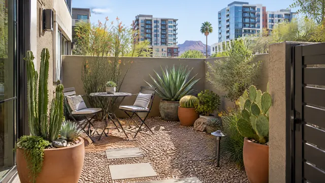 Small courtyard garden of a downtown Tempe, Arizona townhome with potted desert plants, gravel and a bistro table, mid-rise buildings beyond